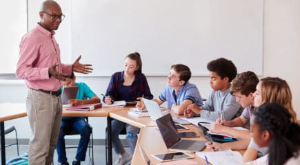 High School Teacher Talking To Pupils Using Digital Devices In Technology Class